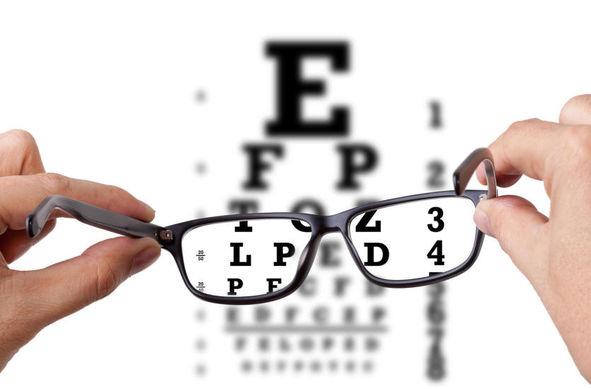 Tablica z rozmytymi literami i dłonie trzymające okulary w których widać litery wyraźnie