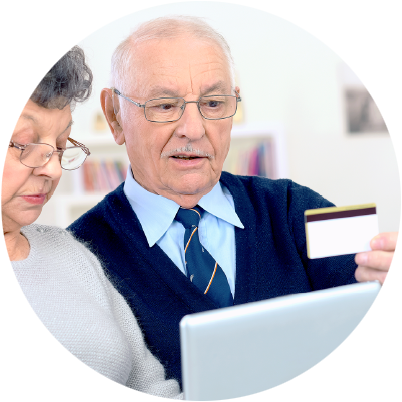 Starszy mężczyzna i starsza kobieta korzystają z komputera, mężczyzna trzyma w ręce kartę płatniczą